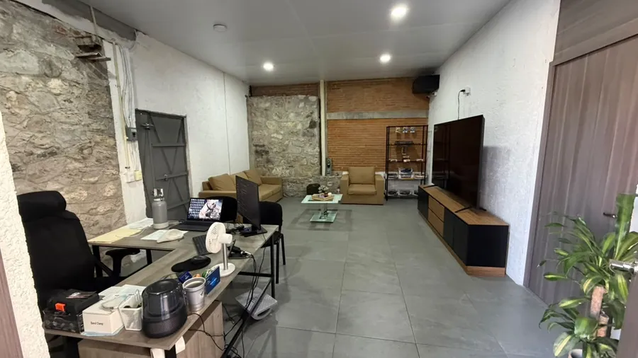 Sala de espera con sillones, pantalla y muro de piedra.