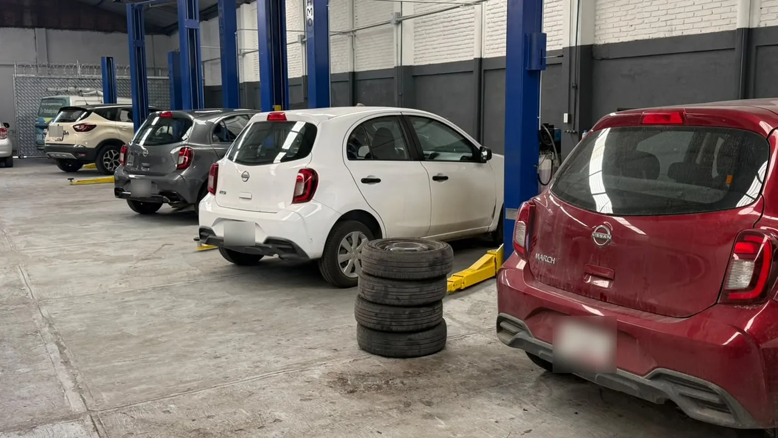 Bahías de servicio de la nave de RAXSA en Puebla: elevadores de dos postes azules, unidades en servicio y un juego de llantas al centro.